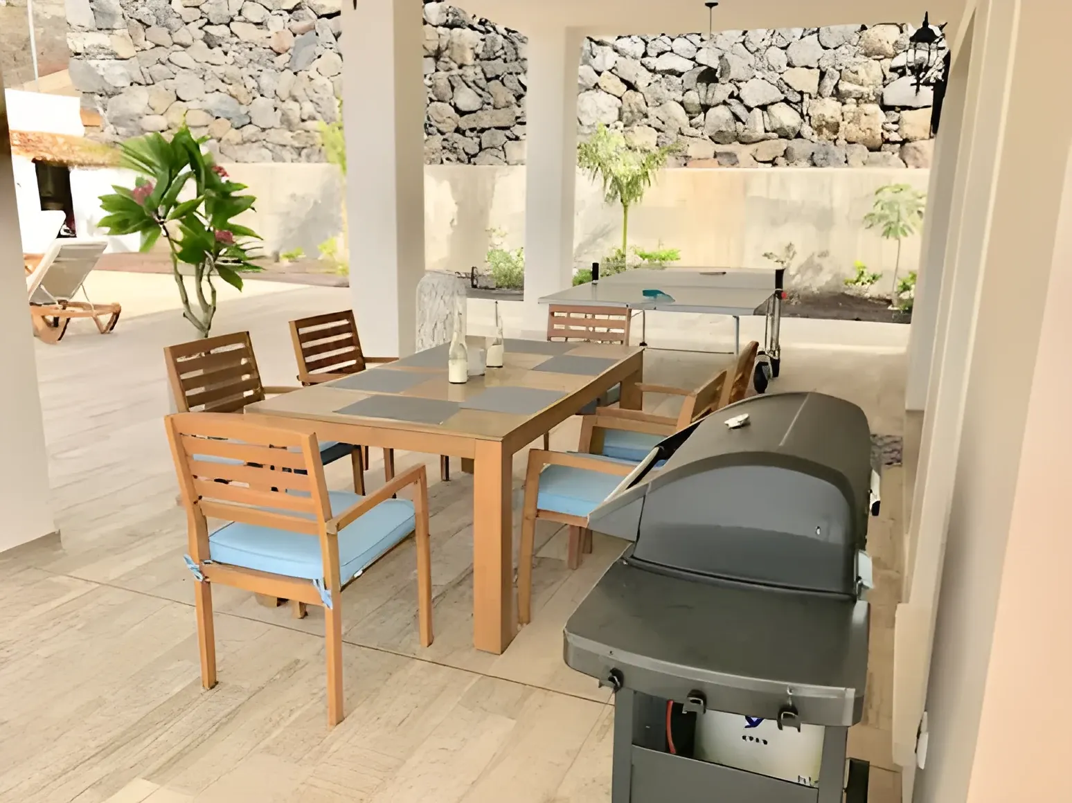 Zona de barbacoa con mesa de comedor exterior bajo el porche